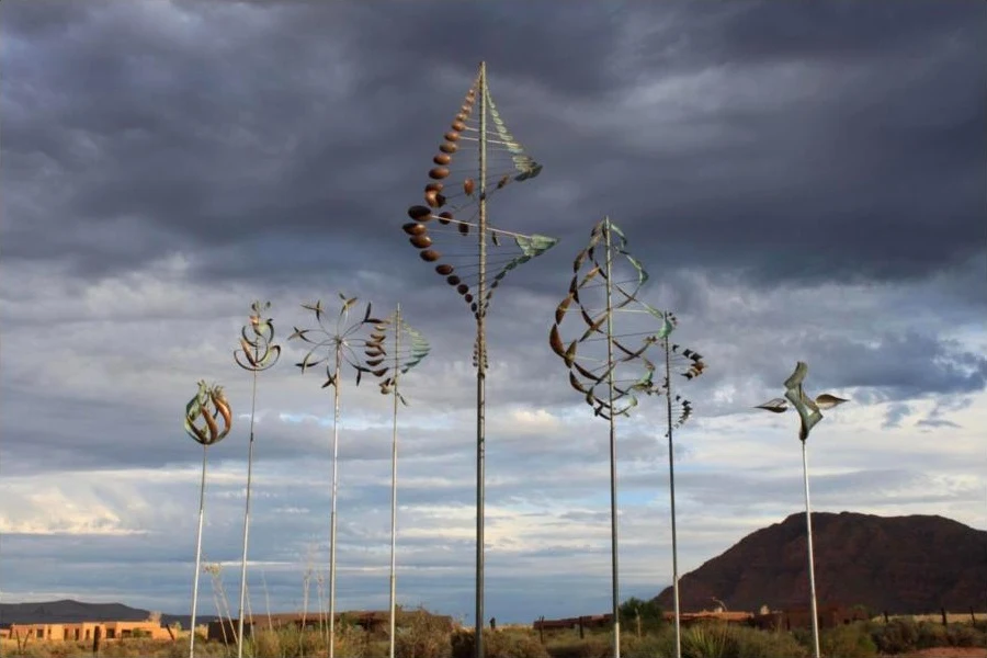 A collection of Whitaker Studio kinetic wind sculptures against a dramatic storm sky near a red-rock landscape