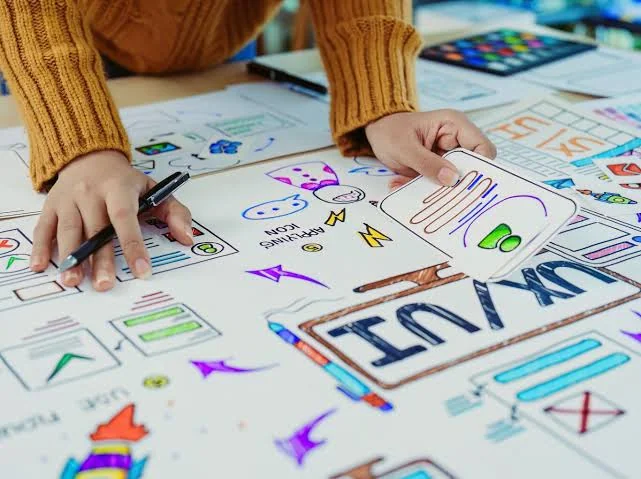 Designer hand-sketching UX wireframes and app icons on paper during a persona and strategy session